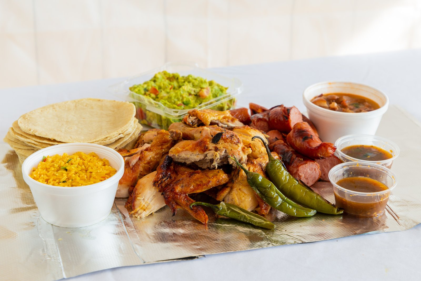 Pollo asado plate at Korner Market — grilled chicken, sausage, Mexican rice, tortillas, guacamole, and salsas